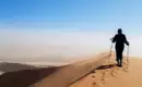 Wandern auf den Dünen von Sossusvlei Person wandert mit Stöcken über eine Sanddüne in der Wüste Sossusvlei.