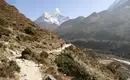 Wanderer auf Bergpfad unterhalb des Himalayas Eine Person wandert auf einem Bergpfad mit schneebedeckten Himalaya-Gipfeln im Hintergrund.