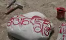 Mani Steine mit tibetischen Inschriften Mani Stein mit roten tibetischen Inschriften auf Sandboden, umgeben von Werkzeugen.