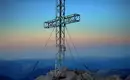 Gipfelkreuz auf dem Dachstein Ein Gipfelkreuz bei Sonnenuntergang auf einem Berg, umgeben von Bergen.