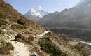 Wanderer auf Bergpfad unterhalb des Himalayas Eine Person wandert auf einem Bergpfad mit schneebedeckten Himalaya-Gipfeln im Hintergrund.