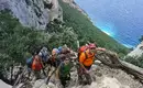 Die letzten Meter bis zum Gipfel - vor einer Traumkulisse Gruppe von Wanderern auf klarem Pfad an steiler Küste Sardiniens.