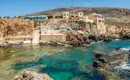 Malerisches Küstendorf auf Malta Blick auf ein maltesisches Küstendorf mit felsiger Küste und klarer See.