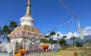 Bunte Stupa in Nepals Landschaft Bunte Stupa im Himalaya mit Gebetsfahnen und Blumen im Vordergrund, blauer Himmel im Hintergrund.