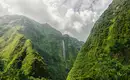 Tropische Landschaft auf La Réunion Grüner Talkessel und Wasserfall auf La Réunion unter bewölktem Himmel.