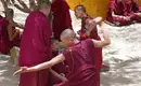 Tibet: Meditierende Mönche im Freien Mehrere Mönche in roten Roben meditieren und diskutieren im Schatten eines Baumes.