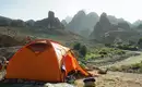 Ein orangefarbenes Zelt in einem steinigen, bergigen Gelände im Hoggar-Gebirge.