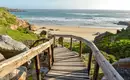 Strandzugang in Südafrika Holzsteg führt zu einem malerischen Strand in Südafrika, umgeben von Felsen und Meerblick.