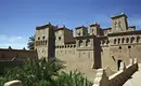 Kasbah in der Straße der 1000 Kasbahs Traditionelle Lehmburg mit dekorativen Mustern und Palmen im Vordergrund.
