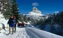 Die Dolomiten: bei Sonne einfach am Schönsten! Menschen beim Schneeschuhwandern vor einer verschneiten Berglandschaft in den Dolomiten.
