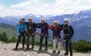 Unsere kleine Klettersteiggruppe, bereits perfekt ausgerüstet, jetzt geht's los! Fünf Kletterer in Kletterausrüstung auf einem Bergpfad mit Alpenpanorama.