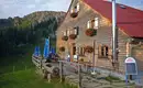Unsere erste Nacht verbringen wir auf der Gundalpe Eine rustikale Berghütte, Gundalpe, mit Blumen am Balkon, umgeben von Bergen.