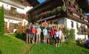 Helden auf Tour! Wandergruppe vor einem traditionellen Alpenhaus mit Holzfassade und Blumen