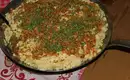 Käsespätzle in der Pfanne serviert - mmhhh Leckere Käsespätzle mit Röstzwiebeln in einer schwarzen Pfanne, garniert mit Schnittlauch, auf einem Holztisch serviert.