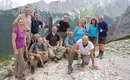Tolle Leistung und Glückwunsch: sie haben es alle geschafft! Gruppe von Wanderern posiert auf einem Bergpfad mit alpiner Kulisse im Hintergrund.