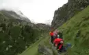 Wandergruppe auf Alpentrail Wandergruppe auf einem schmalen Pfad in den Alpen, umgeben von grüner Landschaft und Bergen.