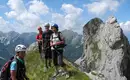 Verdiente kleine Pause vor dem Einstieg in die Vertikale Gruppe von Kletterern auf einem gepflegten Pfad in den Dolomiten mit Berglandschaft im Hintergrund.