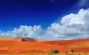 Rote Dünen in der Namib-Wüste Leuchtend rote Sanddünen vor einem blauen Himmel in der Namib-Wüste, Namibia, mit vereinzelten Wolken.
