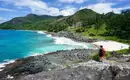 Wanderer auf malerischer Küstenklippe Person steht auf einer Felsklippe mit Blick aufs Meer und Strand auf den Seychellen.