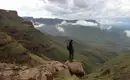 Was für ein toller Ausblick in den Drakensbergen. Eine Person steht auf einem Felsen mit Blick über grüne Berghänge und Wolken in den Drakensbergen.
