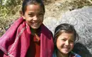 Freundliche Begegnung im Himalaya Zwei lächelnde Kinder in traditioneller Kleidung in einer Berglandschaft.