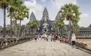 Angkor Wat - Kambodschas ikonischer Tempelkomplex Besucher betreten Angkor Wat vor Palmen und blauem Himmel.