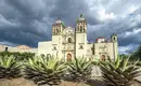 Kolonialarchitektur in Mexiko Historische Kirche in Oaxaca, umgeben von Kakteen unter dramatischem Himmel.