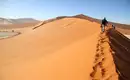 Wanderung in der Namib-Wüste Personen wandern auf einer Sanddüne in der Namib-Wüste unter klarem Himmel.