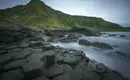 Basaltsäulen am Giant's Causeway Hexagonale Basaltsäulen am Ufer mit grünem Hügel im Hintergrund