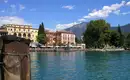 Die Uferpromenade von Riva del Garda Blick auf bunte Gebäude in Riva del Garda am Ufer des Gardasees mit Bergen im Hintergrund.