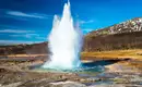 Ein beeindruckender Geysir-Ausbruch in Islands Landschaft, umgeben von Bergen.