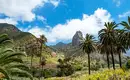 Majestätische Landschaft La Gomera: Im Hintergrund der Roque Agando Palmen und grüne Hügel vor einem beeindruckenden Berg auf La Gomera.