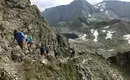Wanderetappe in den Schladminger Alpen Gruppe von Wanderern auf schmalem Pfad in bergiger Landschaft mit See im Hintergrund.