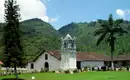 Was für ein Kontrast: Kleine Kirche in tropischer Landschaft Eine kleine, weiß getünchte Kirche vor grünen, bewaldeten Hügeln und Palmen.