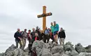 Gipfelsieg auf der Wanderung Eine Gruppe von Wanderern posiert auf einem steinigen Gipfel neben einem hölzernen Gipfelkreuz.