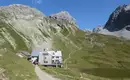 Unser nächstes Etappenziel in greifbarer Nähe! Eine Berghütte in alpiner Landschaft mit Bergpfaden und grünen Hängen.