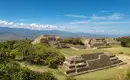 Maya-Ruinen von Monte Albán Maya-Ruinen von Monte Albán; steinige Terrassen und Pyramiden in üppiger Landschaft unter blauem Himmel.