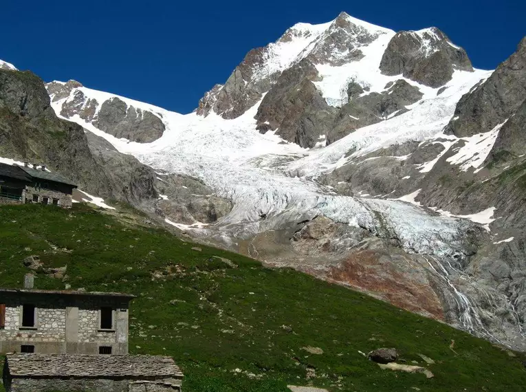 Schneebedeckte Gipfel des Mont Blanc und steinernes Bergchalet in grüner Alpenlandschaft.