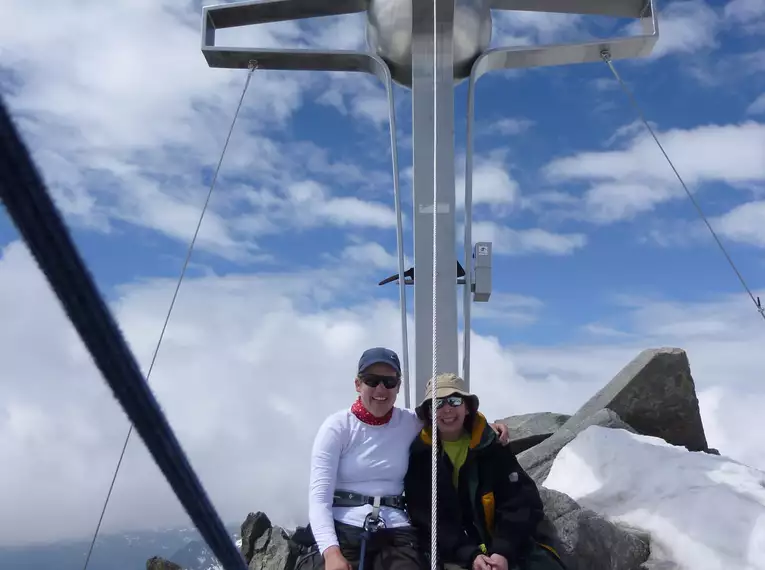 Zwei Bergsteiger am Gipfelkreuz des Zuckerhütl in den verschneiten Stubaier Alpen. Abenteuerliche Hochtour mit fantastischer Aussicht.