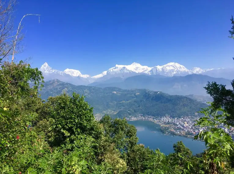 Atemberaubende Aussicht auf das Annapurna-Massiv in Nepal mit üppiger Vegetation im Vordergrund und einem klaren blauen Himmel.
