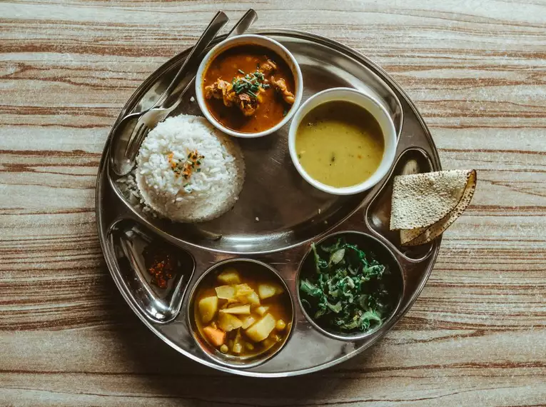 Traditionelles nepalesisches Dal Bhat Ein Teller mit Dal Bhat und Beilagen auf einer Holzoberfläche.