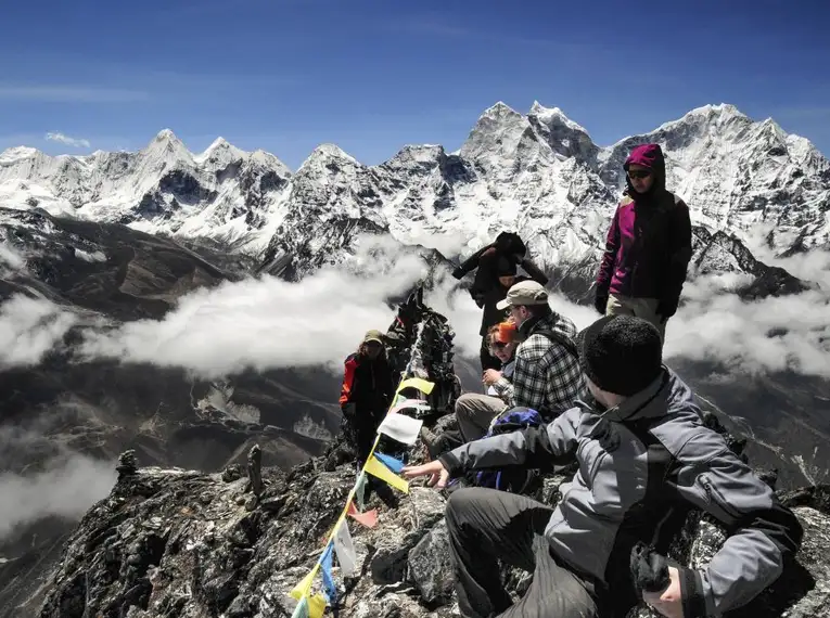 Reisegruppe im Himalaya vor schneebedeckten Bergen und Gebetsfahnen.