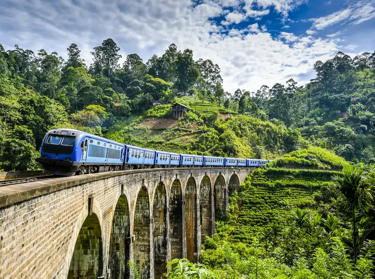 Ein blauer Zug überquert eine Brücke in Sri Lankas grüner Landschaft.