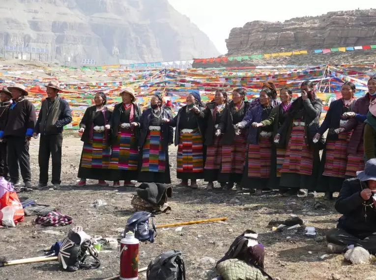 Gruppe von Pilgern in traditioneller Kleidung vor bunten Gebetsfahnen in Tibet.