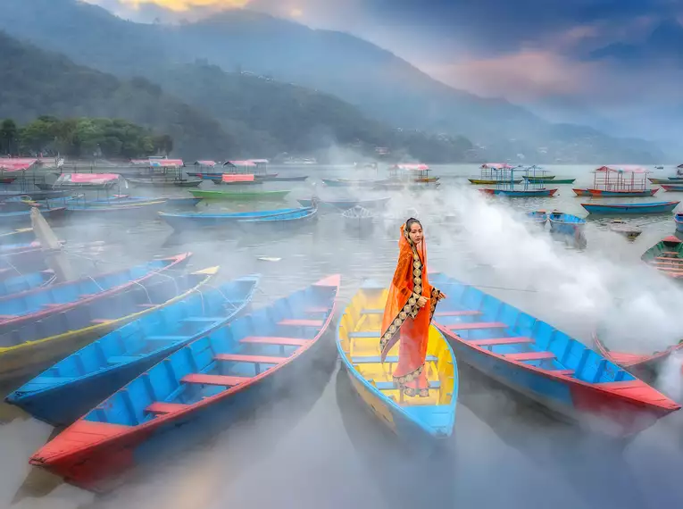 Bootsfahrt auf dem Phewasee Farbige Boote am Phewasee, Nepal mit Frau im traditionellen Gewand.