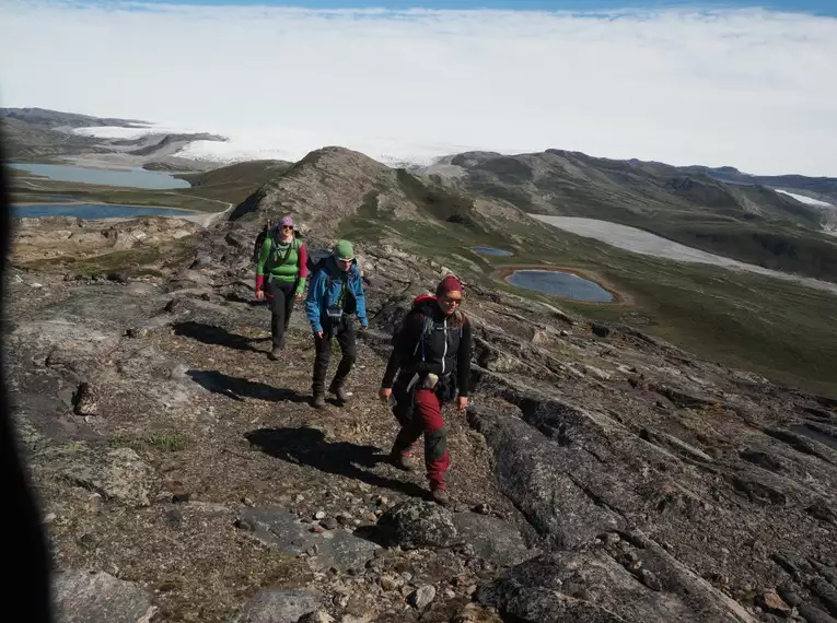 Wanderer auf Grönlands Bergpfaden Drei Wanderer in der arktischen Landschaft Grönlands mit Bergseen und Gletscher im Hintergrund.