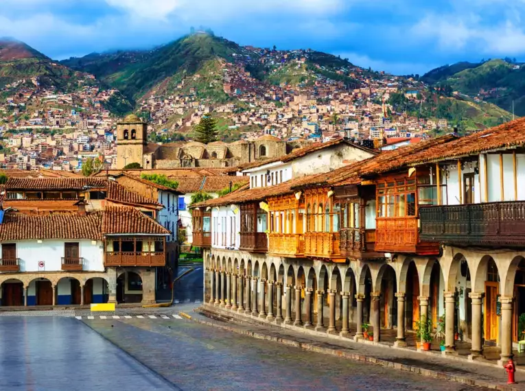 Historische Gebäude und Arkaden in Cusco, Peru vor einer Bergkulisse.