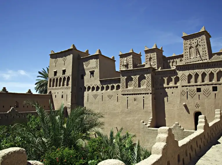 Kasbah in der Straße der 1000 Kasbahs Traditionelle Lehmburg mit dekorativen Mustern und Palmen im Vordergrund.