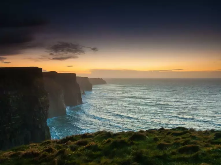 Was für ein Küstenpanorama bei Sonnenuntergang! Steilküste in Irland bei Sonnenuntergang mit Meerblick und dramatischem Himmel.