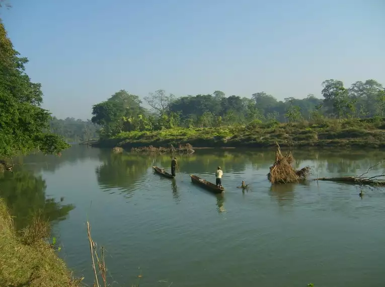Einbaumfahrt im Chitwan-Nationalpark Zwei Einbäume auf einem Fluss im Chitwan-Nationalpark, umgeben von üppiger Vegetation.